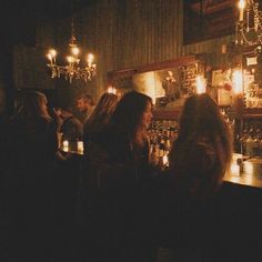 people are sitting at a bar with candles on the wall and chandeliers hanging from the ceiling