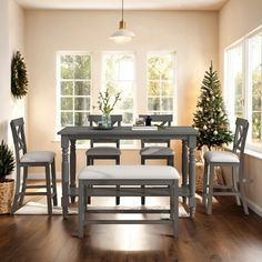 a dining room table with chairs and bench in front of two potted christmas trees