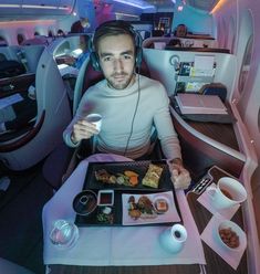 a man sitting at a table with food and headphones on in an airplane cabin