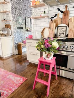 a pink stool sitting in front of a stove top oven next to a wooden floor