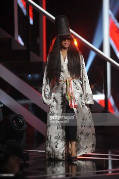 the woman is walking down the runway wearing a long coat and black hat with flowers on it