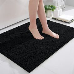 a woman standing on top of a black rug in a bathroom next to a bathtub