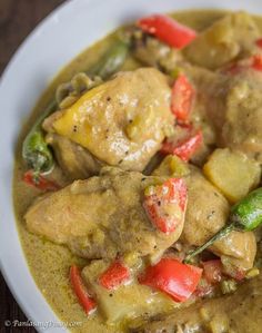 a white plate topped with chicken and veggies covered in gravy on top of a wooden table