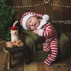 a baby is sleeping on a chair next to a christmas tree and cookies, while wearing a santa hat