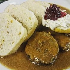 a white plate topped with meat covered in gravy next to bread and cranberry sauce