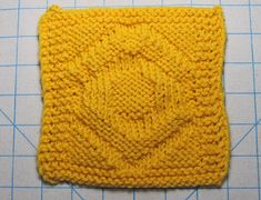 a yellow knitted square sitting on top of a cutting board