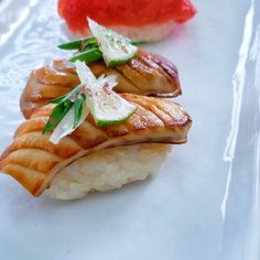 three sushi dishes on a white plate with sauces and garnishes