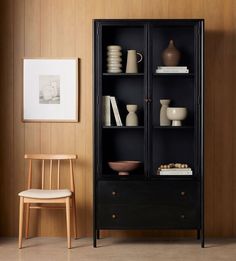 a black bookcase sitting next to a wooden chair in front of a brown wall