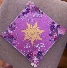 a purple and yellow graduation cap with flowers on the side that says, flows when my life begins