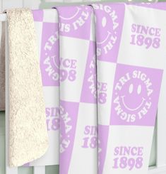 three towels hanging from the side of a white crib with purple and white designs