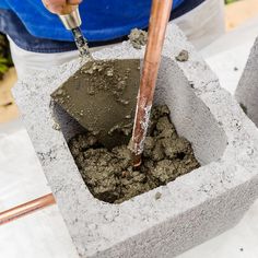 a person pouring cement into a concrete block with a wooden stick sticking out of it