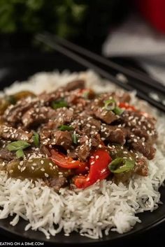 a black plate topped with rice and meat covered in sesame seeds, peppers and green onions