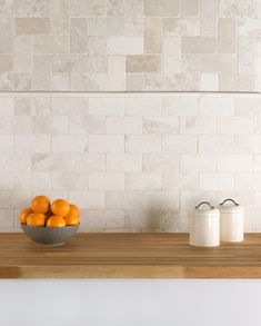 a bowl of oranges sitting on top of a wooden counter next to two salt shakers