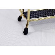 a small black and gold stool with wheels on it's legs, sitting on a white surface