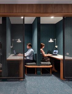 a man and woman sitting at a desk in an office cubicle with green walls