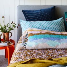 a bed with colorful pillows on top of it next to an orange table and potted plant