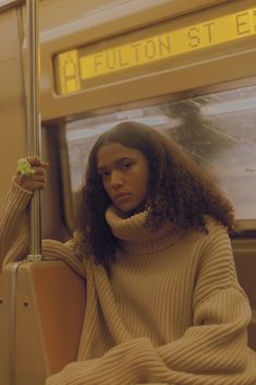 a woman sitting on a train holding onto a pole