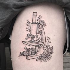 a black and white tattoo design of a microscope with flowers on it's thigh