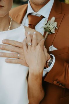 a bride and groom holding each other's wedding rings with their hands on their chest