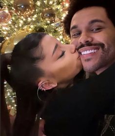 a man and woman kissing in front of a christmas tree