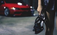 a woman holding a purse standing next to a red car