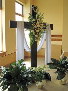 a cross decorated with flowers and greenery in front of a window at a church