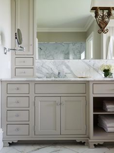 a large bathroom with marble counter tops and white cabinetry, along with a chandelier