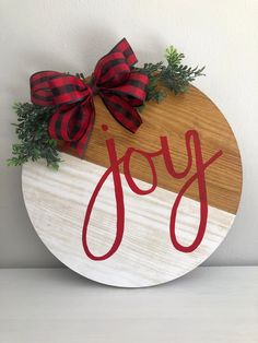 a wooden sign with the word joy painted on it and a red bow tied to it