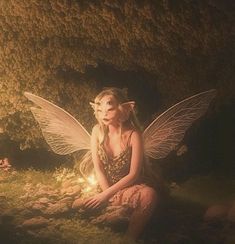 a fairy sitting on the ground next to a tree with lights in its hands and her eyes closed