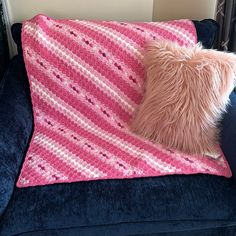 a pink and white blanket sitting on top of a blue couch next to a pillow