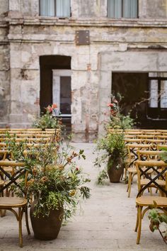 rows of wooden chairs and tables with flowers on them in front of an old building