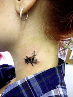 a woman's neck with a small bee tattoo on it