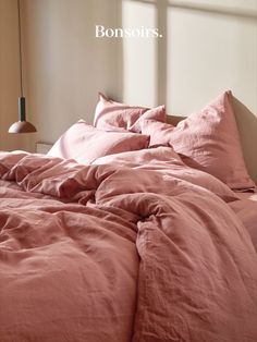 an unmade bed with pink linens and a lamp on the nightstand next to it