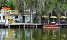 there is a boat that is in the water near some buildings and trees with yellow umbrellas