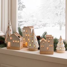 a window sill decorated with christmas lights and small houses in front of a snowy landscape