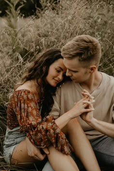 a young man and woman sitting in tall grass looking into each other's eyes