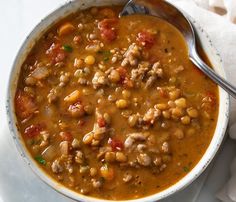 a white bowl filled with beans and meat on top of a table next to a napkin