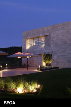 a modern house lit up at night with lawn and umbrellas in the foreground