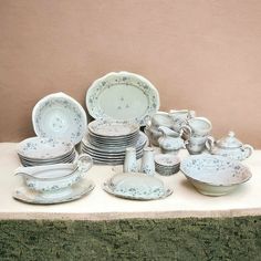 a table topped with lots of white dishes and cups on top of a green cloth