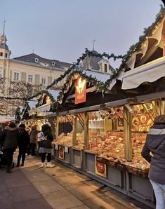 people are walking around an outdoor market with christmas decorations on the roof and in front of it