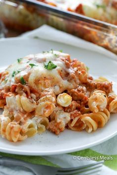 a white plate topped with pasta and meat covered in sauce next to a casserole dish