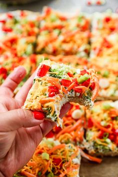 someone holding up a slice of pizza with veggies and cheese on it in front of the rest of the pizza