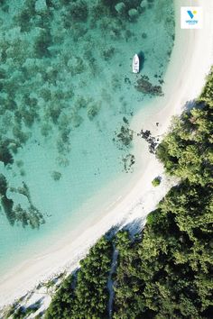 an aerial view of a beach with a boat in the water and trees surrounding it