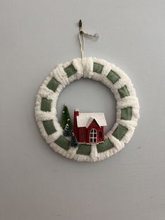 a christmas ornament hanging on the wall with a house and trees in it