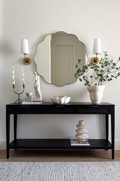 a black console table with white vases and candles on it in front of a mirror