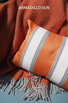 an orange and white striped pillow sitting on top of a blanket