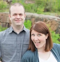 a man and woman standing next to each other in front of some rocks with trees