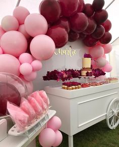 a table with pink and red balloons, cake and desserts on the table in front of it