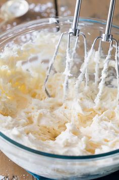 a mixing bowl filled with whipped cream on top of a wooden table next to a whisk attachment