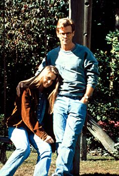 a man and woman standing next to each other in front of a wooden pole with trees behind them